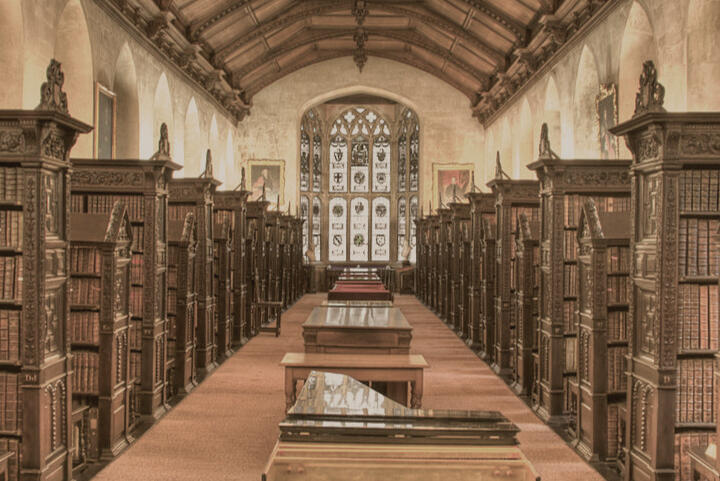 A university library with wooden bookshelves and ornate glass windows.